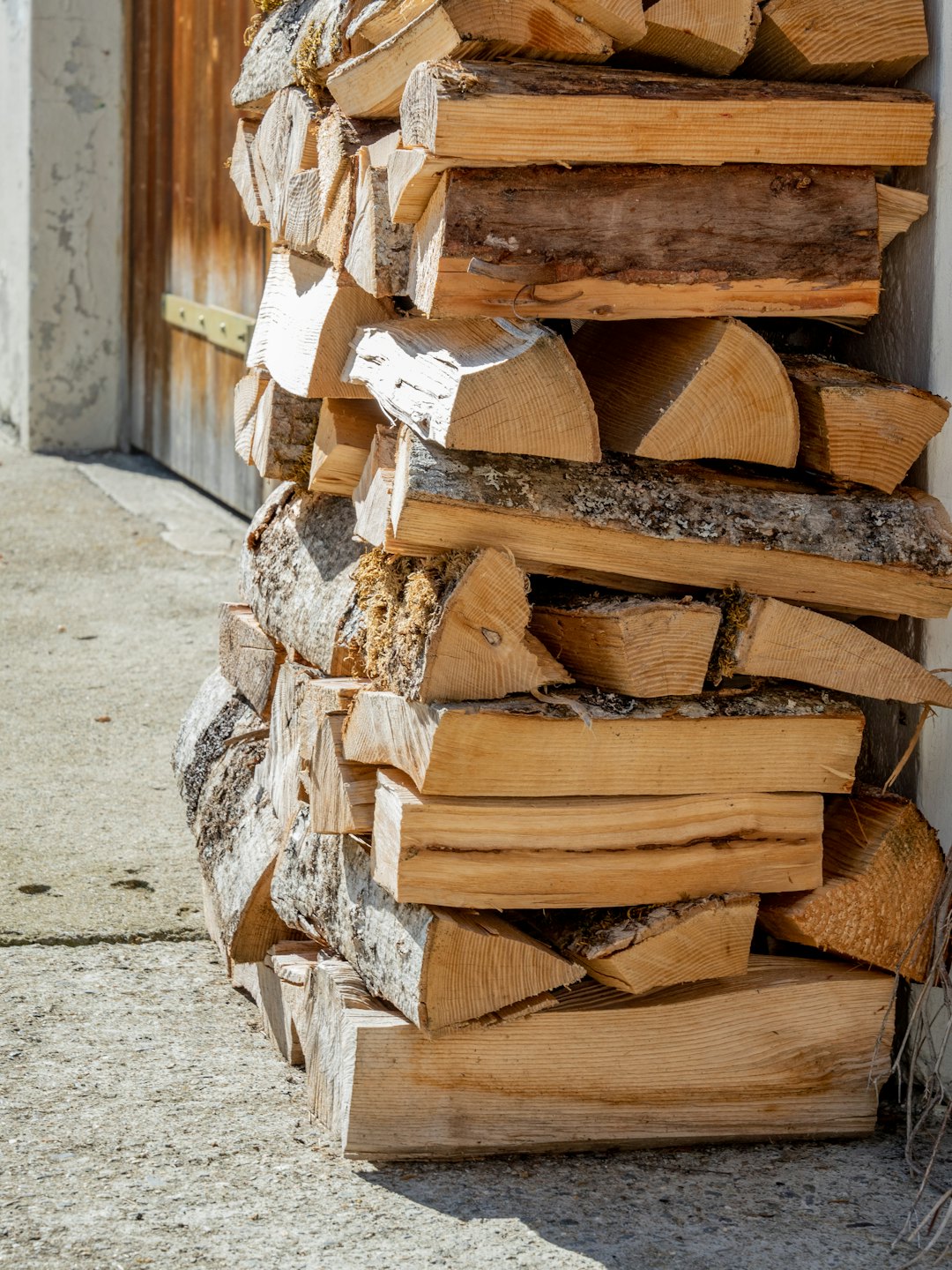 Des bûches de bois empilées s'appuient contre un mur et une porte en bois.