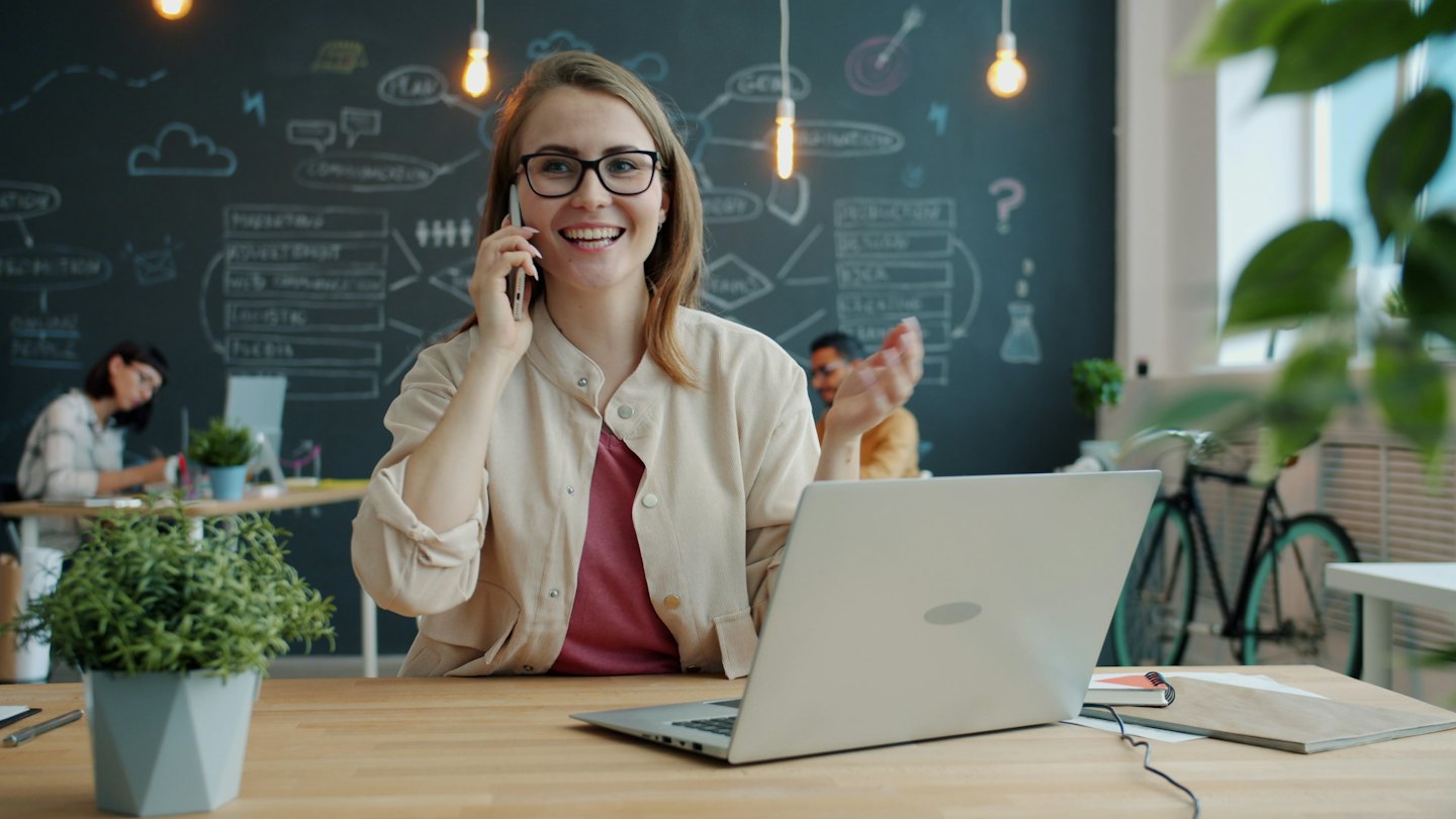 Femme avec des lunettes parle au téléphone dans un bureau moderne.