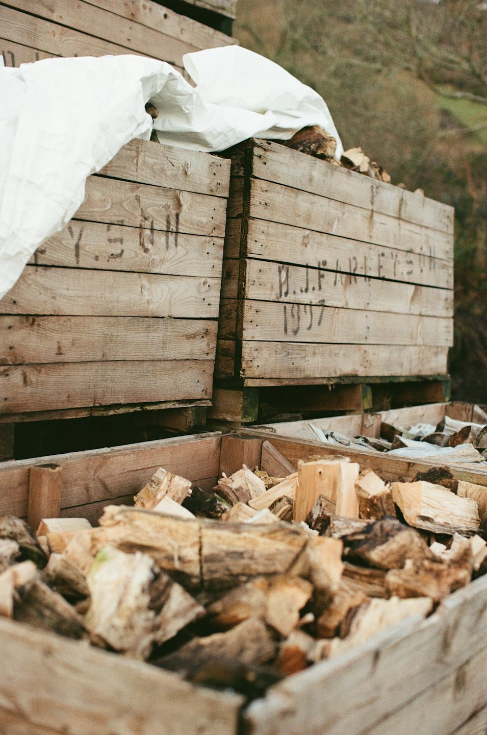Des caisses en bois empilées remplies de bûches coupées et de bois de chauffage à l'extérieur.