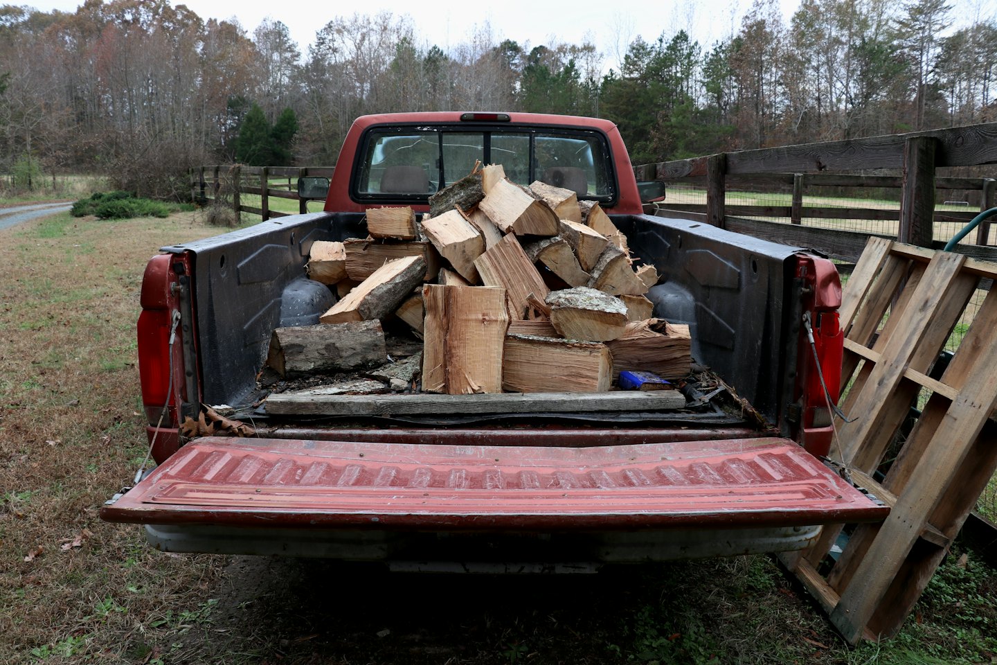 Camionnette rouge, hayon ouvert, remplie de bûches de bois de chauffage.