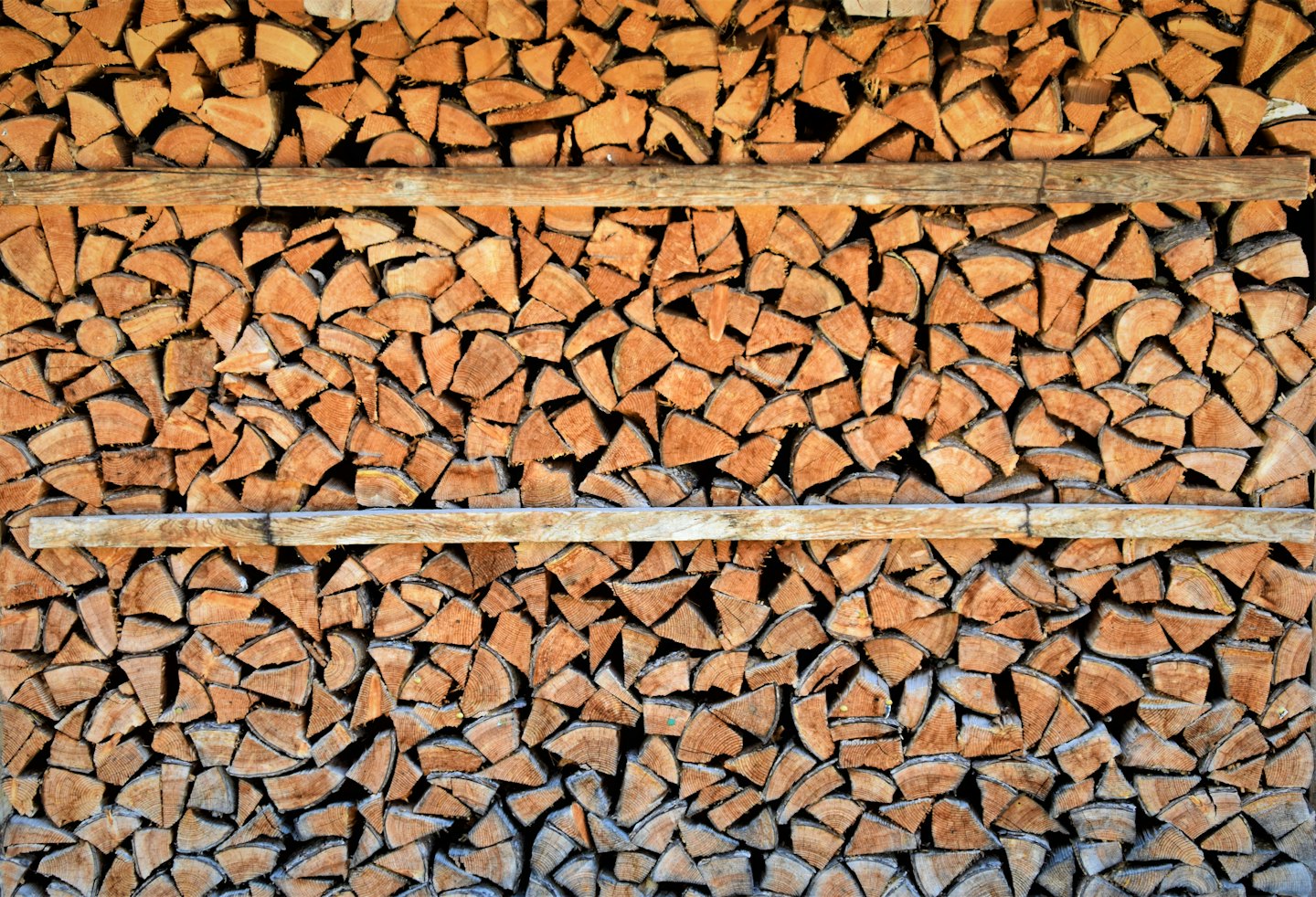 Bois de chauffage coupé, empilé proprement entre des poutres de support horizontales en bois.