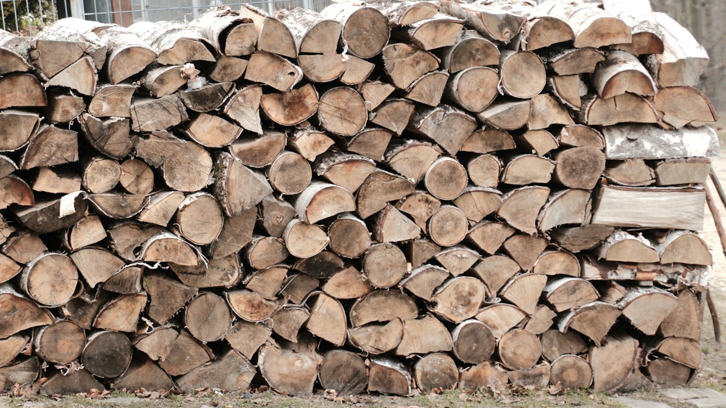 Gros tas de bois de chauffage fendu, bien empilé sur l'herbe.