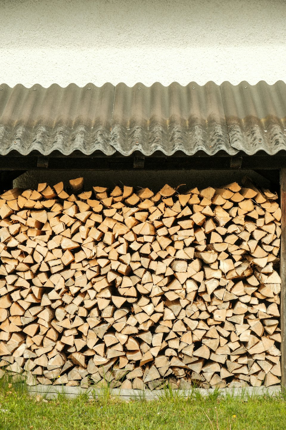 Bûches de bois de chauffage empilées sous un toit métallique à l'extérieur.
